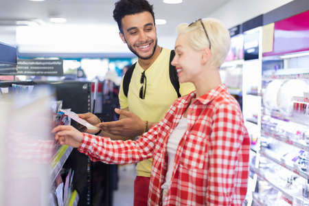Young Couple In Supermarket Choosing Products Happy Smiling Man And Woman Buying Cosmetics Shop Interiorの写真素材