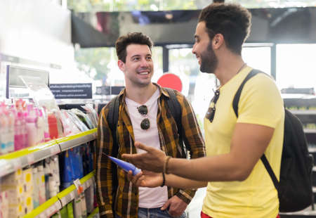 Young Man Couple In Supermarket Choosing Products Happy Smiling Guys Buying Shop Interiorの写真素材