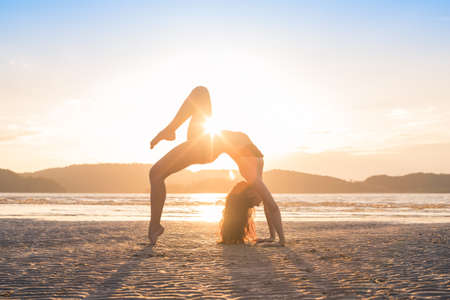 Young Girl Practicing Yoga On Beach At Sunset, Beautiful Woman Summer Vacation Meditation Seaside Sea Ocean Holiday Travelの写真素材