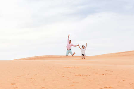Young Man Woman Jump Up In Desert Beautiful Couple Asian Girl And Guy Sand Dune Landscape Backgroundの写真素材
