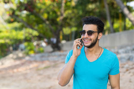 Young Hispanic Man Talking Phone Call Tropical Beach Sea Holiday Guy Summer Vacation Ocean Travelの写真素材