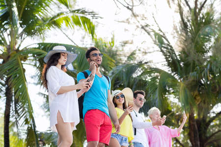Young People Group Using Cell Smart Phones Tropical Park Palm Trees Friends Chatting Online Holiday Summer Vacation Ocean Travelの写真素材