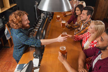 Young People Group In Bar, Barman Friends Sitting At Wooden Counter Pub, Drink Beer Communication Party Celebrationの写真素材