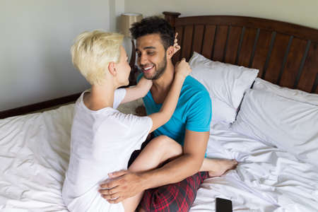 Young Couple Lying On Bed, Happy Smile Hispanic Man And Woman Embrace Bedroom Hotel Room Interiorの写真素材