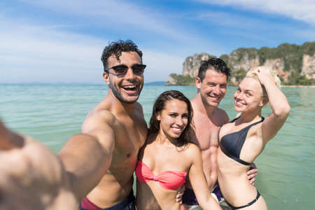 Young People Group On Beach Summer Vacation, Happy Smiling Friends Taking Selfie Photo In Water Sea Ocean Holiday Travelの写真素材