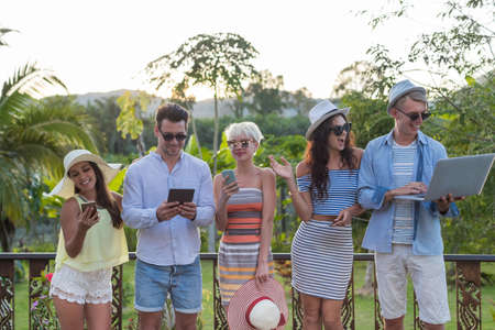 Young People Group On Terrace Tropical Hotel, Friends Using Cell Smart Phone Tropic Holiday Vacation Green Forestの写真素材