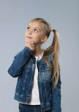 Little Teenage Girl In Jeans Coat, Small Kid Looking Up To Copy Space Think Hold Chin Isolated Over Gray Backgroundの写真素材