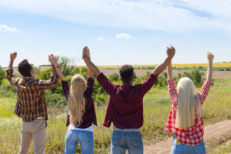 People group outdoor countryside excited raise arms rear back view friends holding hands up summer...