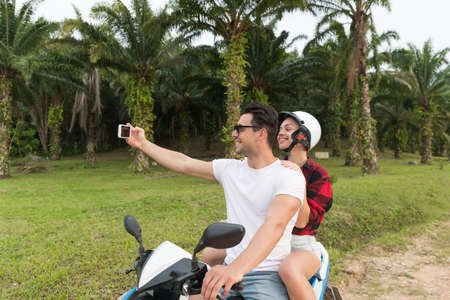 Couple Riding Motorbike, Man And Woman Taking Selfie Travel On Bike On Tropical Forest Road During Exotic Summer Holidayの写真素材