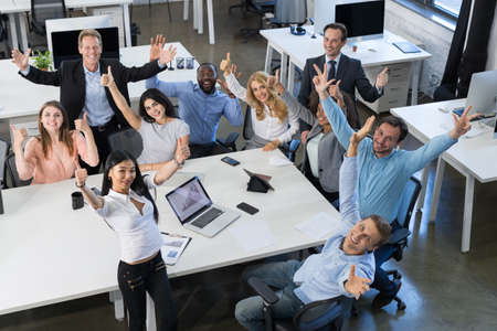 Successful Excited Mix Race Businesspeople Team Sitting At Table On Meeting, Holding Raised Hand...