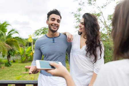 Latin Man And Woman Couple Standing On Summer Terrace Talking With Girl Holding Cell Smart Phone, Young People Over Tropical Forest Landscapeの写真素材