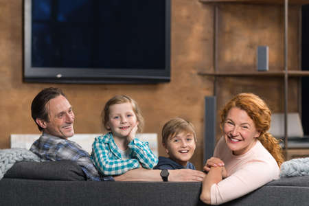 Happy Smiling Family Sitting On Couch In Living Room, Parents Couple With Two Children At Homeの写真素材