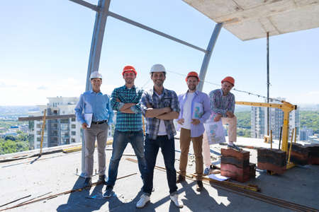 Builders Team Leader With Group Of Apprentices At Construction Site Over City View Background, Happy Smiling Engineersの写真素材