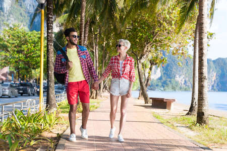 Casual Couple Hold Hands Walking In Tropical Palm Trees Park, Beautiful Young People On Summer Vacation, Latin Man And Blonde Woman Holiday Travelの写真素材