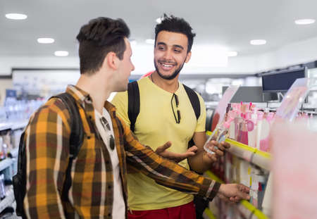 Young Man Couple In Supermarket Choosing Products Happy Smiling Guys Buying Shop Interiorの写真素材