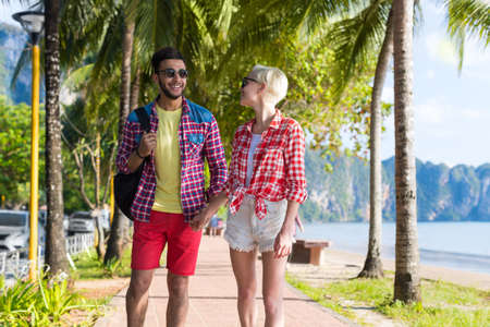 Casual Couple Hold Hands Walking In Tropical Palm Trees Park, Beautiful Young People On Summer Vacation, Latin Man And Blonde Woman Holiday Travelの写真素材