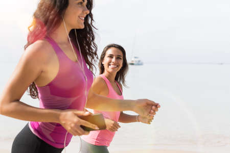 Closeup Of Two Young Woman Jogging On Beach Together Attractive Girls Running On Seaside Sport Runner Fitness Training Outdoors Healthy Lifestyle Conceptの写真素材