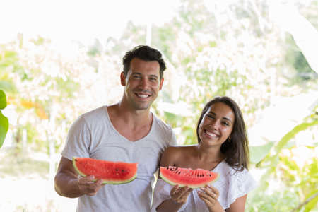 Happy Couple Holding Water Melon Slice In Hands Cheerful Smiling Man And Woman Embrace With Watermelon Outdoors On Summer Terraceの写真素材