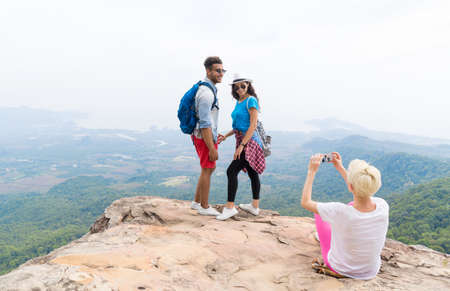 Girl Taking Photo Of Couple With Backpacks Posing Over Mountain Landscape On Cell Smart Phone,...