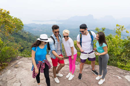 Tourist Group Watch Photos On Cell Smart Phones, People With Backpack Over Landscape From Mountain Top, Young Frineds On Hikeの写真素材