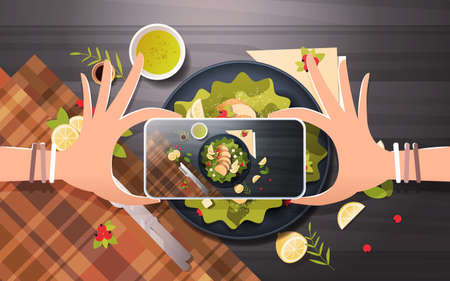 food blogger taking mobile photo of fresh vegetable salad with chicken and sauce in black bowl top...