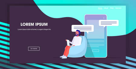 man using laptop computer chatting app social network speech chat bubble communication concept guy sitting on bean bag smartphone screen full length copy space horizontal vector illustrationのイラスト素材