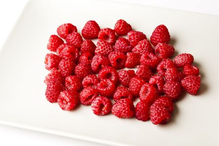 Fresh red raspberries ready to be eaten on a simple white square plate. Isolated on white.の写真素材