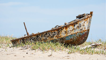 Abandoned boat on sandy shore rested and covered in barnacles leaning to one sideの素材