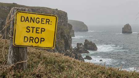 Warning sign Danger Steep Drop at cliffs edge by ocean rocksの素材