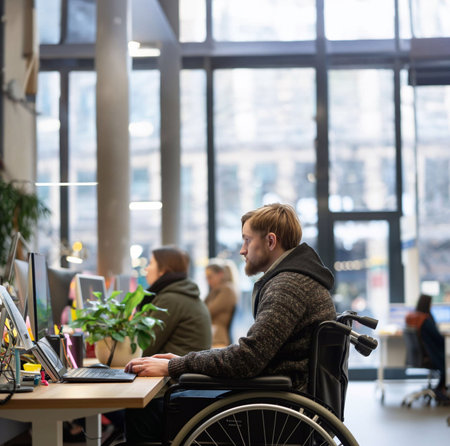 A disabled employee in a wheelchair working with coworkers in an officeの素材