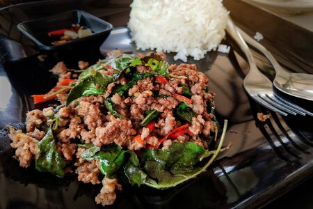 Stir fried chopped meat with chili and basil and  steamed rice on black plateの写真素材