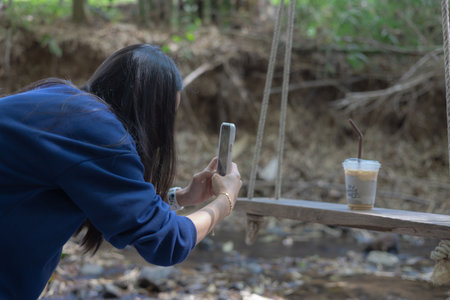 Woman taking photo reviewing coffee by streamの写真素材