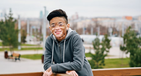 Asian teen with vitiligo smiling outdoors in urban park settingの素材