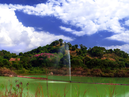 Small pond with a fountain in the background of a rocky hill.の写真素材