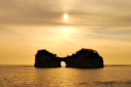Sun setting behind an uniquely shaped island with an opening at the bottomの写真素材