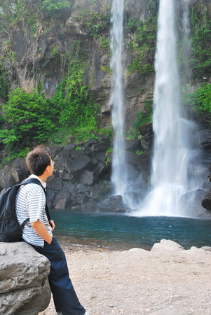 Man resting in front of a majestic waterfall and gazing upの写真素材
