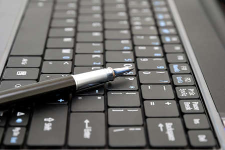 Pen on black laptop keyboard signifying concepts such as electronics and technology, office and business, and work related objects.の写真素材