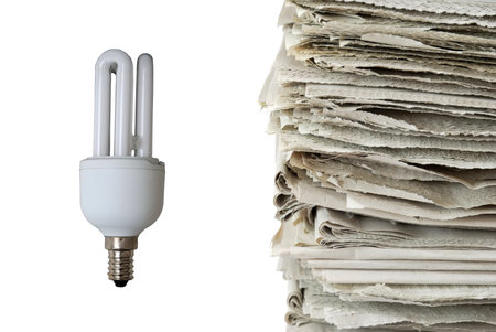Light bulb and stack of old newspapers isolated on white background, signifying energy consumption,...