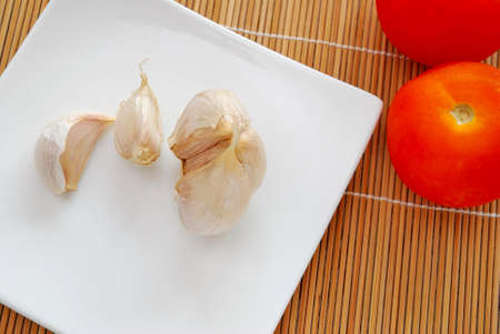 A few garlic cloves on white plate with tomatoes. Commonly used as seasoning and food ingredient in many Chinese cuisine. For food and beverage concepts.の写真素材