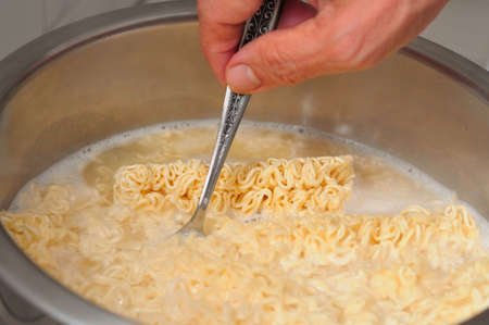 Hand cooking and stirring noodles in cooking pot of boiling water.の写真素材