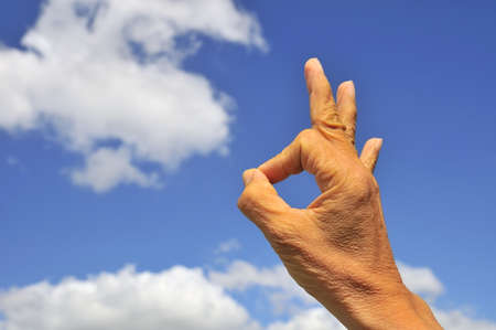 Hand showing okay sign on right of frame with blue sky and cloud background.の写真素材