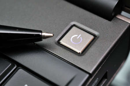 Black pen pointing to lighted up power button on computer.の写真素材