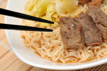Japanese style chopsticks eating tasty yellow noodles with meat pieces.の写真素材