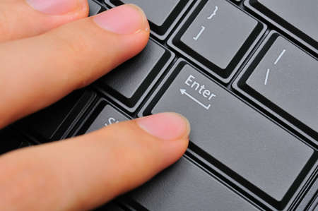 Left hand fingers pressing on black Enter key on computer keyboard.の写真素材
