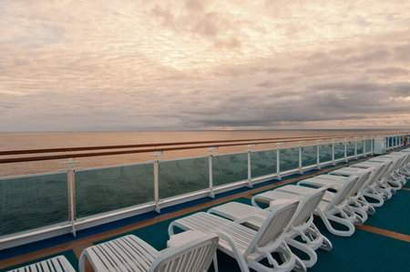 White beach chairs on cruise ship deck overlooking sea.