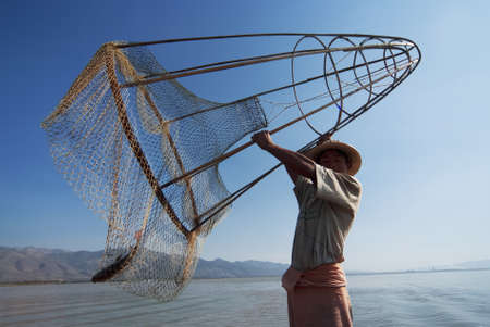 INLE LAKE, MYANMAR - FEBRUARY 16: Fisherman catches fish on February 16, 2011 on Inle Lake, Myanmar. The traditional fishing method is to use a long coop with net.のeditorial素材