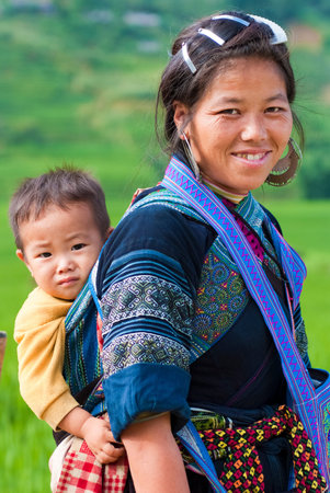 SAPA, VIETNAM â JULY 6: Hmong woman carries her child on the back on July 6 2009 in Sapa, Vietnam.  Hmong women are known for their indigo-dyed costumes and wrap long scarves around their legs.のeditorial素材