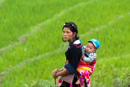 SAPA, VIETNAM â JULY 6: Hmong woman carries her child on the back on July 6 2009 in Sapa, Vietnam.  Black Hmong women are known for their indigo-dyed costumes and wrap long scarves around their legs.のeditorial素材