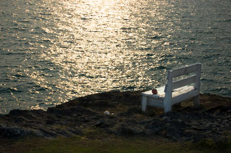 A sole chair on a cliff protruding out to the sea at sunsetの写真素材