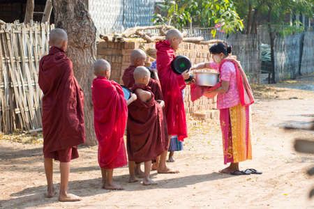 BAGAN, MYANMAR â MAR 2: A woman gives alms to novice monks on Mar 2, 2015 in Bagan, Myanmar. This behavior can be seen everyday in any village.のeditorial素材